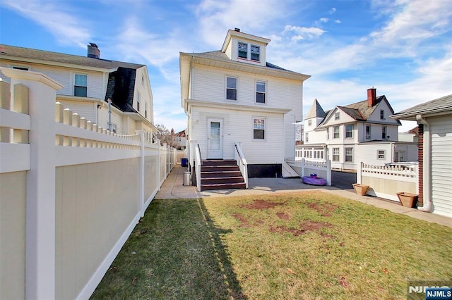 back of house with a fenced backyard, a lawn, and a residential view