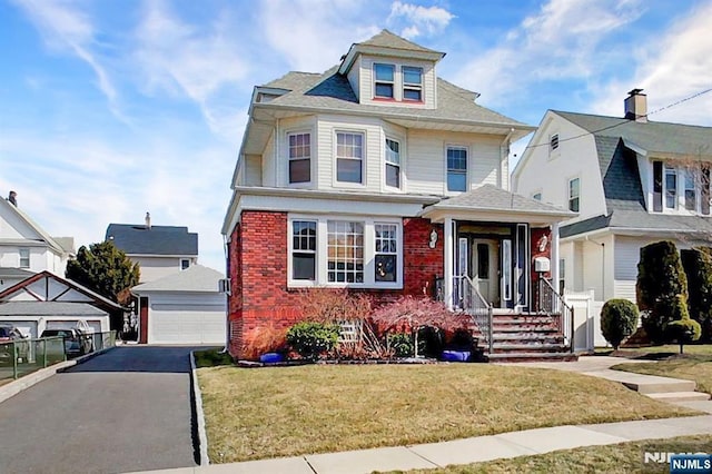 american foursquare style home with a detached garage, brick siding, an outdoor structure, and a front lawn