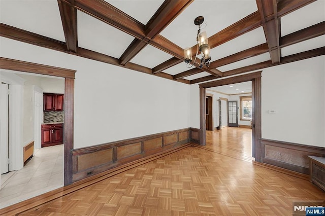 empty room with radiator, a wainscoted wall, coffered ceiling, an inviting chandelier, and beamed ceiling