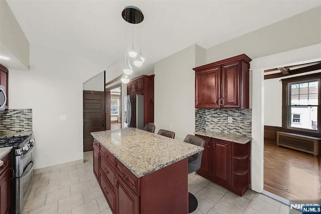 kitchen featuring reddish brown cabinets, a kitchen island, appliances with stainless steel finishes, and light stone countertops