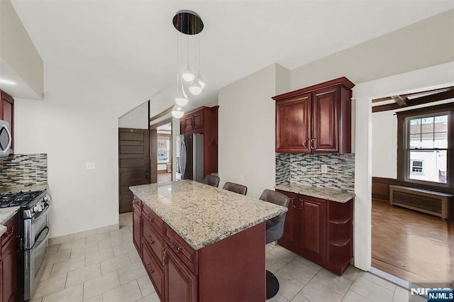 kitchen featuring reddish brown cabinets, a kitchen island, appliances with stainless steel finishes, and light stone countertops