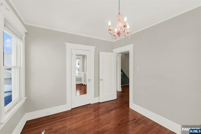 empty room featuring wood finished floors, a notable chandelier, a healthy amount of sunlight, and baseboards