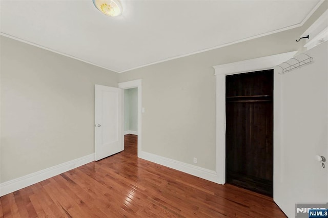 unfurnished bedroom with baseboards, wood-type flooring, a closet, and ornamental molding