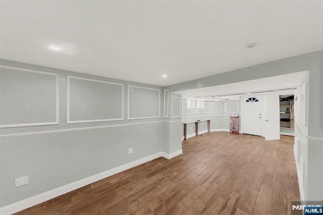 finished below grade area with a decorative wall, recessed lighting, wood finished floors, and baseboards