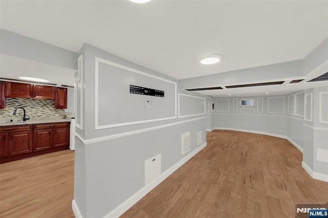 hallway with a sink, light wood-type flooring, baseboards, and visible vents