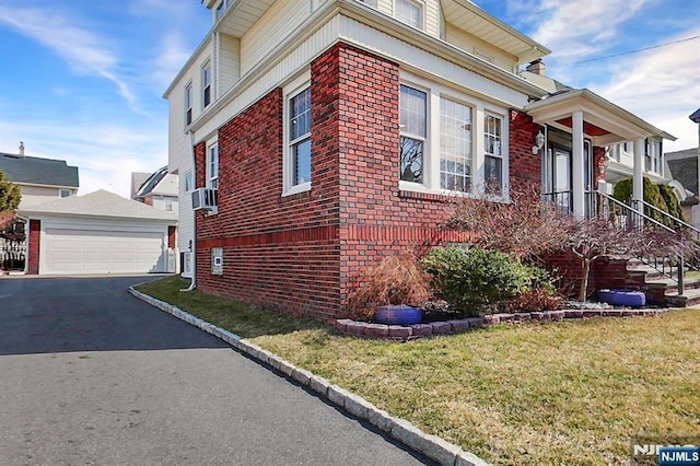 view of property exterior with brick siding, a detached garage, an outbuilding, and a yard