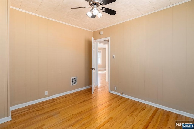 empty room featuring visible vents, baseboards, ornamental molding, light wood-style flooring, and a ceiling fan