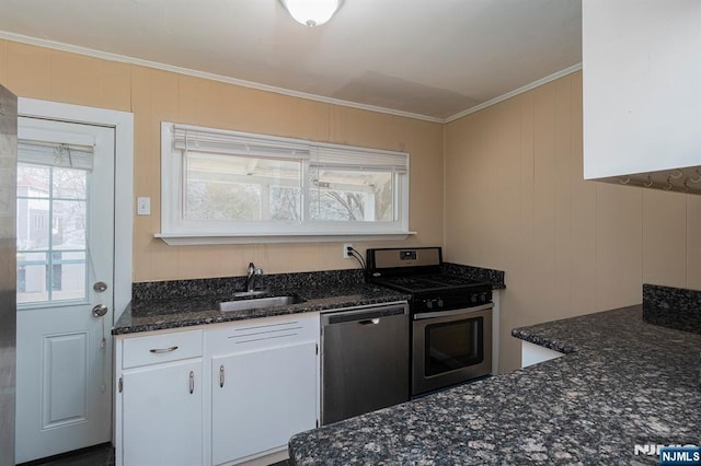 kitchen featuring dark stone counters, ornamental molding, a sink, appliances with stainless steel finishes, and white cabinetry