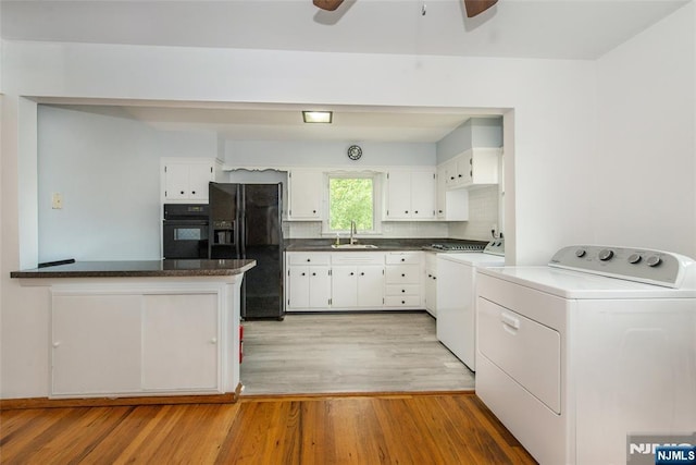 kitchen with washing machine and clothes dryer, light wood finished floors, dark countertops, black appliances, and a sink