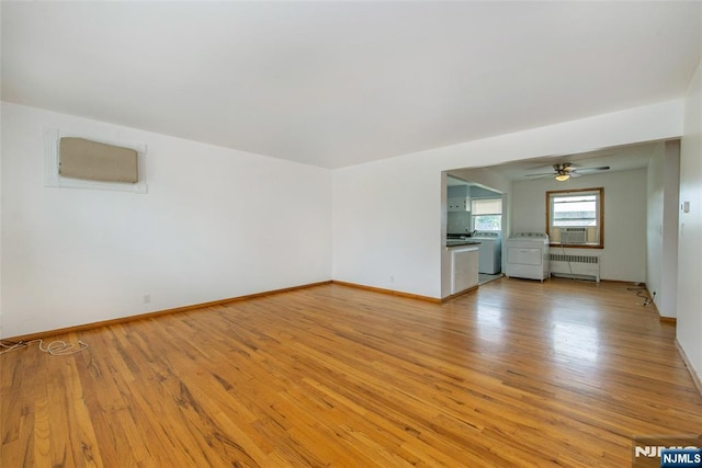 empty room with baseboards, washer / dryer, light wood-style flooring, and radiator heating unit