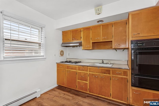 kitchen featuring wood finished floors, a baseboard radiator, a sink, stainless steel gas stovetop, and under cabinet range hood