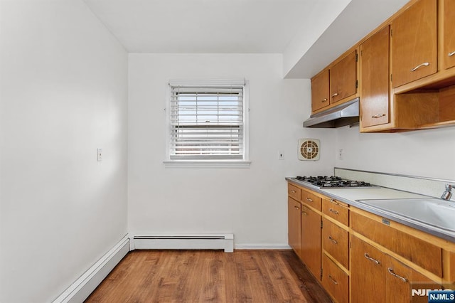 kitchen with brown cabinets, under cabinet range hood, a sink, dark wood finished floors, and baseboard heating