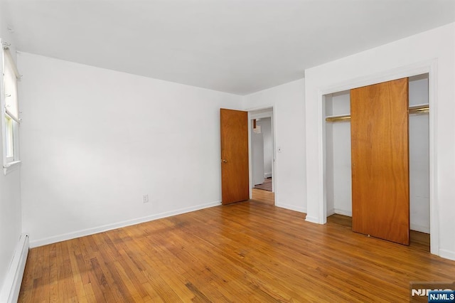 unfurnished bedroom featuring a closet, light wood-type flooring, baseboards, and a baseboard radiator