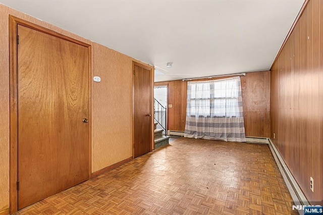 unfurnished room featuring stairway, wood walls, and a baseboard heating unit