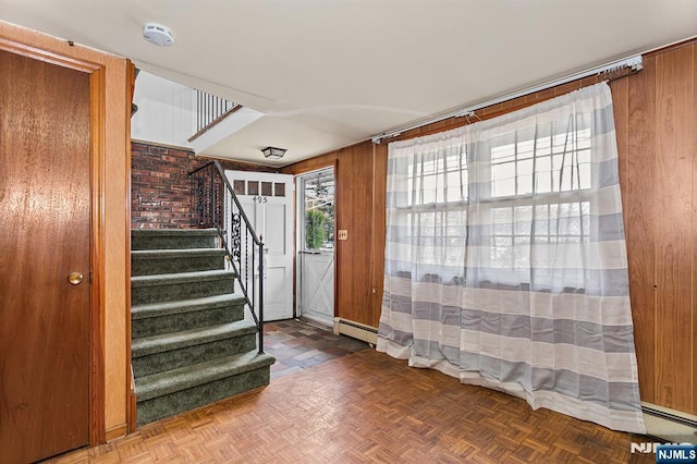 foyer entrance featuring stairway, baseboard heating, and wood walls