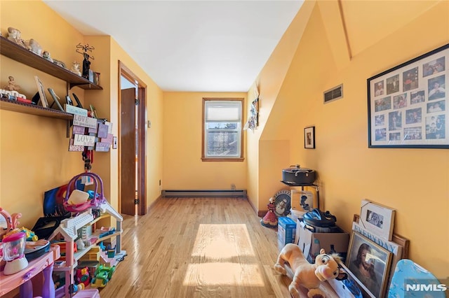 interior space with a baseboard heating unit, wood finished floors, and visible vents