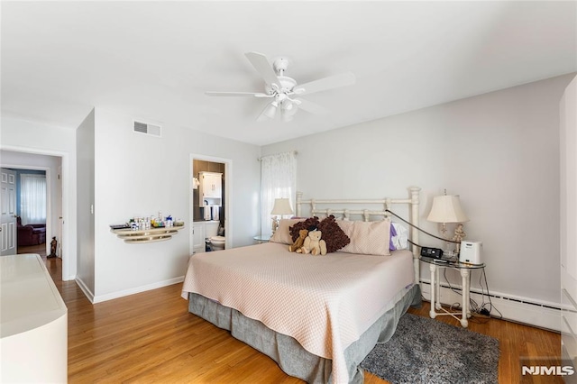 bedroom with wood finished floors, visible vents, baseboard heating, and baseboards