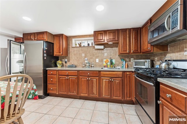 kitchen with a sink, appliances with stainless steel finishes, light tile patterned flooring, light countertops, and decorative backsplash