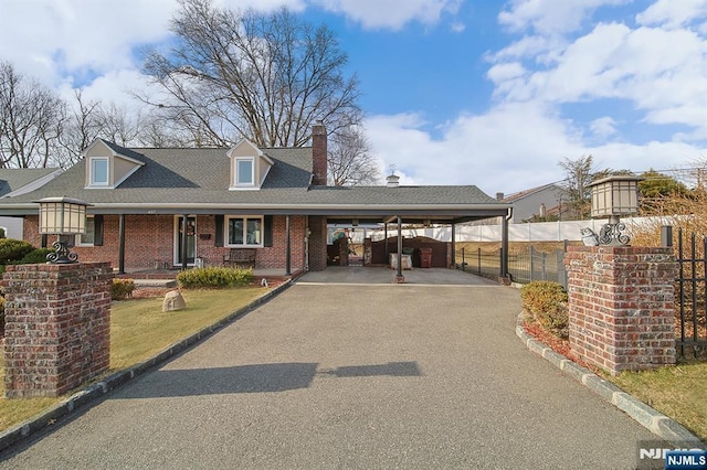 view of front of house featuring aphalt driveway, a carport, fence, brick siding, and a chimney