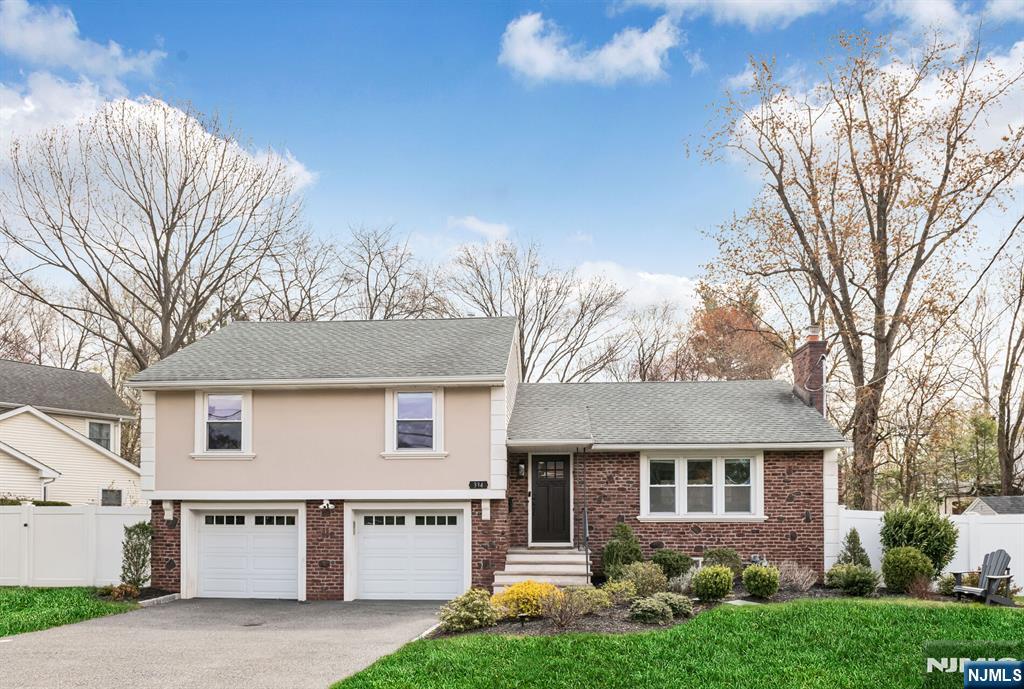 tri-level home featuring fence, an attached garage, a chimney, and aphalt driveway