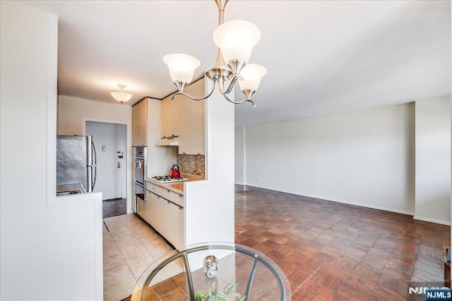 kitchen featuring tasteful backsplash, white gas stovetop, light countertops, freestanding refrigerator, and a notable chandelier