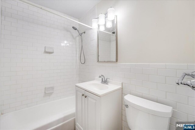 full bathroom featuring a wainscoted wall, toilet, tile walls, and vanity