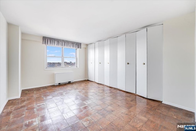 unfurnished bedroom featuring two closets, baseboards, and radiator