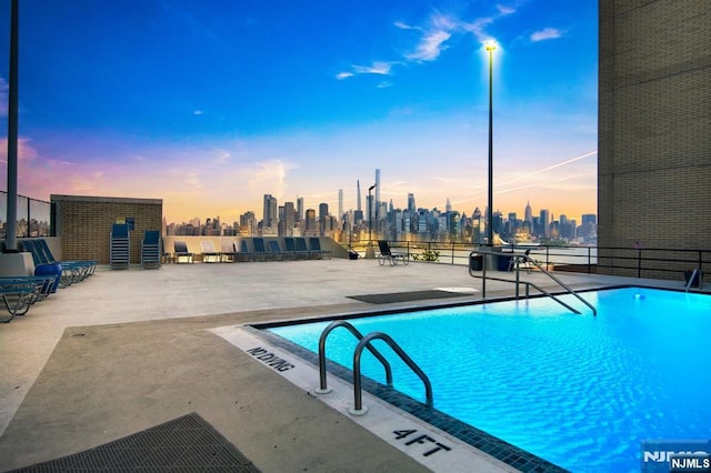 pool at dusk featuring a city view, a community pool, and a patio area