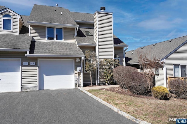 townhome / multi-family property with a garage, driveway, roof with shingles, and a chimney