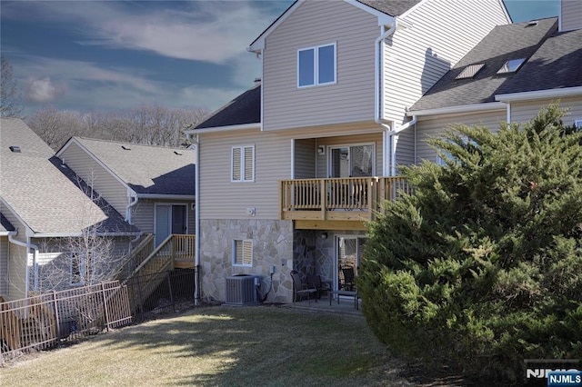 rear view of house featuring a balcony, cooling unit, fence, stone siding, and a lawn