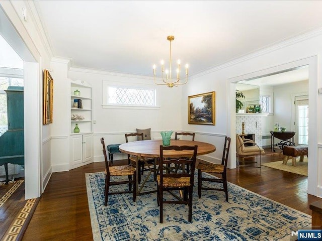 dining area featuring built in features, dark wood-style flooring, a chandelier, and ornamental molding