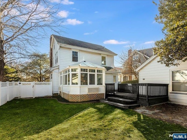 back of property with a fenced backyard, a deck, a yard, and a sunroom