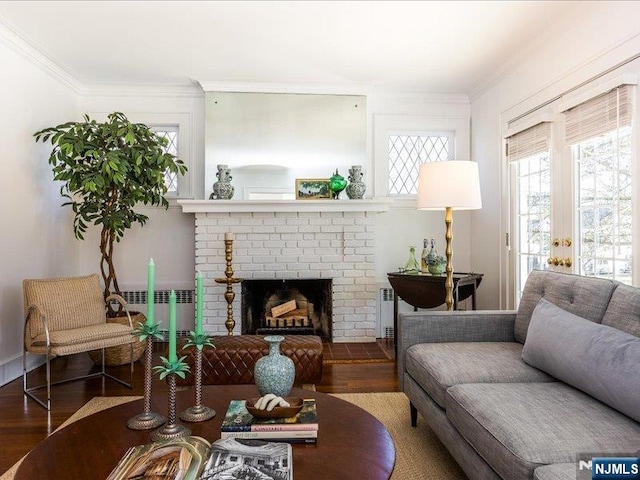 living room featuring wood finished floors, radiator, a brick fireplace, and ornamental molding