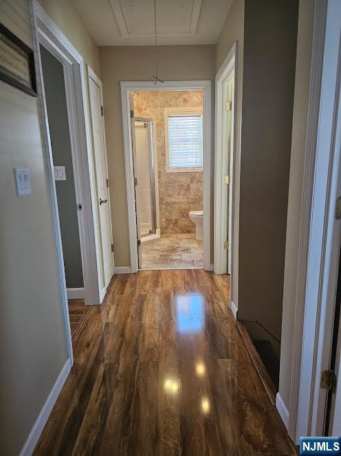 hallway featuring attic access, baseboards, and wood finished floors