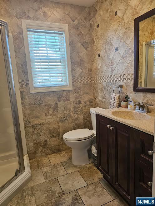 bathroom with toilet, tile walls, a stall shower, and vanity