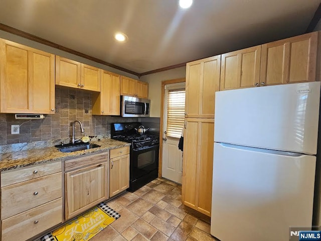 kitchen with stainless steel microwave, black gas stove, light brown cabinets, freestanding refrigerator, and a sink