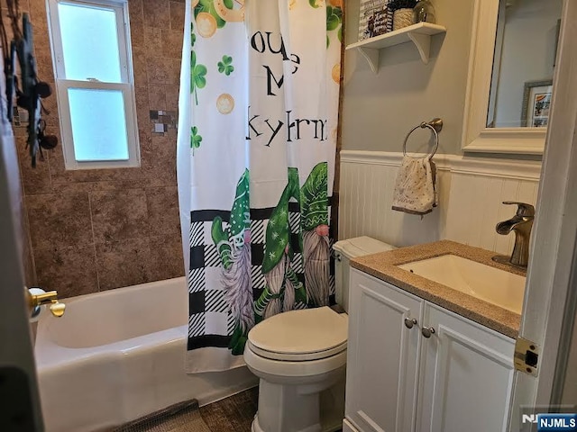 full bath with vanity, shower / tub combo, toilet, and wainscoting