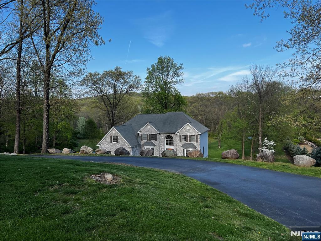 view of front of home with a front yard, a view of trees, and stone siding