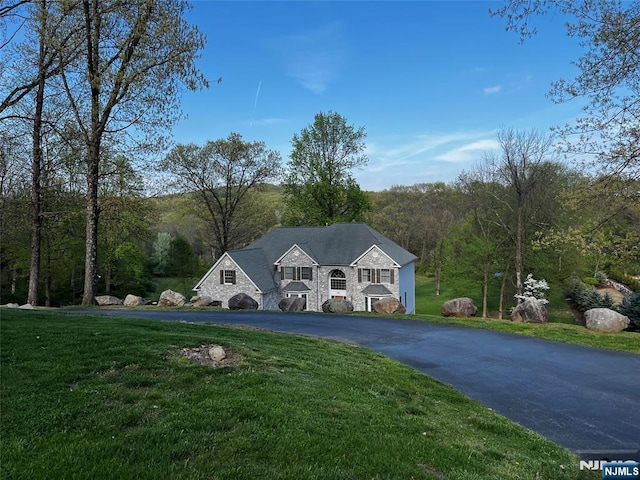 view of front of home with a front yard, a view of trees, and stone siding