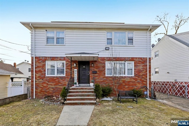 view of front of home with brick siding, a front lawn, and fence