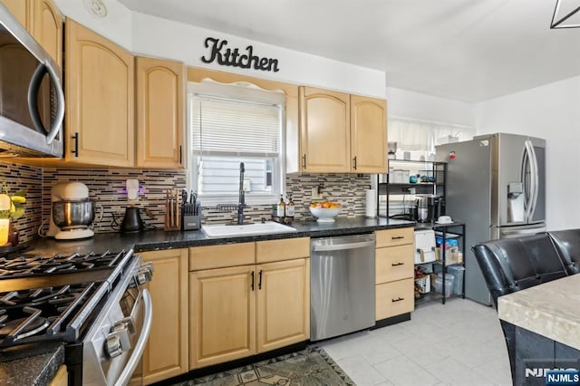 kitchen featuring a sink, decorative backsplash, light brown cabinetry, appliances with stainless steel finishes, and dark countertops