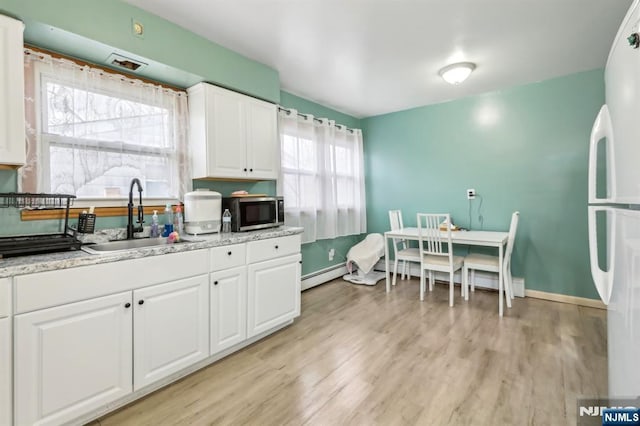 kitchen featuring a sink, white cabinetry, stainless steel microwave, light wood-type flooring, and a baseboard heating unit