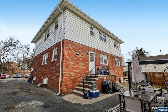 rear view of house featuring brick siding, a patio, and fence