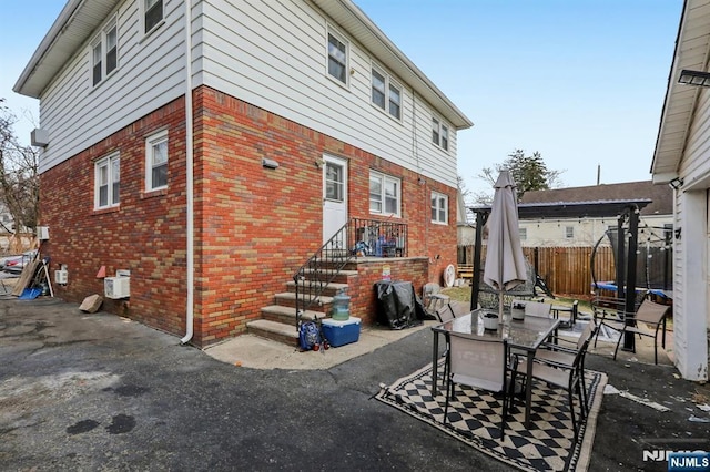 back of house featuring a patio, a trampoline, brick siding, and fence