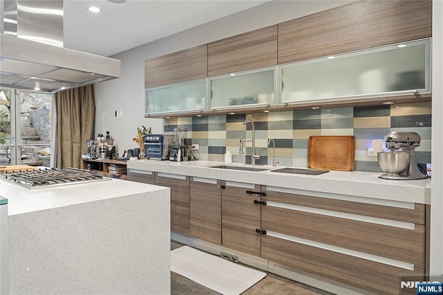 kitchen featuring modern cabinets, a sink, tasteful backsplash, stainless steel gas stovetop, and island range hood