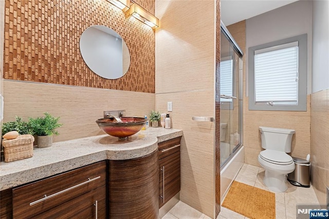 full bath featuring tile patterned floors, toilet, tile walls, bath / shower combo with glass door, and vanity