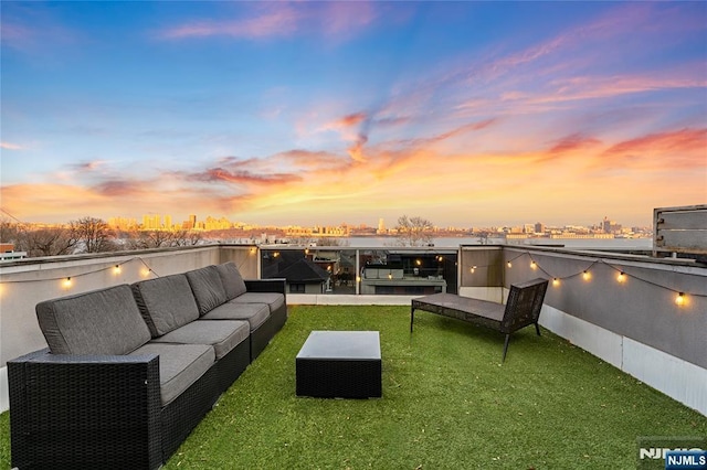 patio terrace at dusk featuring a lawn, outdoor lounge area, and a water view