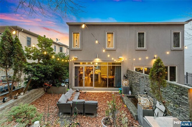 back of house at dusk featuring stucco siding and fence