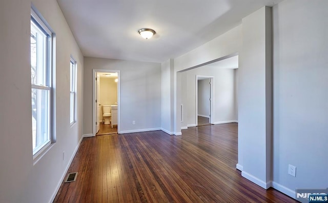 empty room featuring dark wood-style floors, visible vents, and baseboards