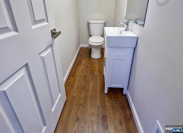 half bathroom with baseboards, toilet, wood finished floors, and vanity